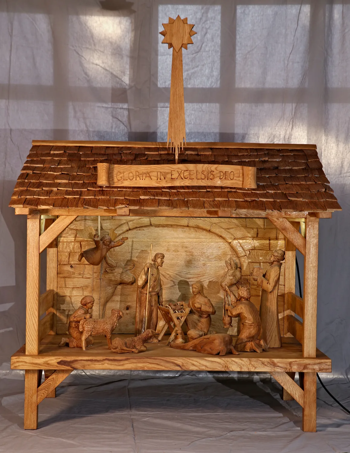Dubový betlém se šindelovou střechou, kometou a páskou Gloria in excelsis Deo, s reliéfním pozadím a vyřezávanými figurami