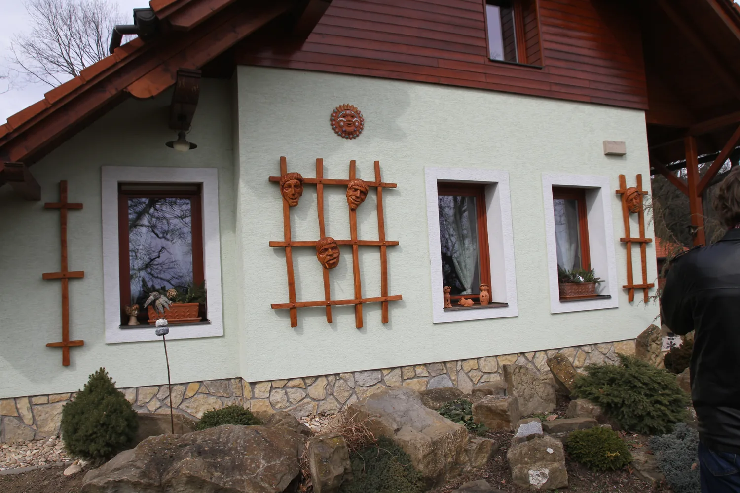 Dřevěné mříže s vyřezanými tvářemi na fasádě rodinného domu