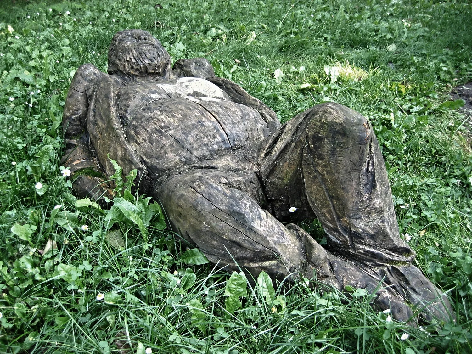 Ležící dřevěná socha v trávě, zahradní socha zestárlá v exteriéru